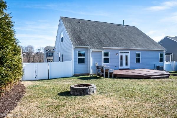 back of property featuring a lawn, a wooden deck, central AC, and a fire pit