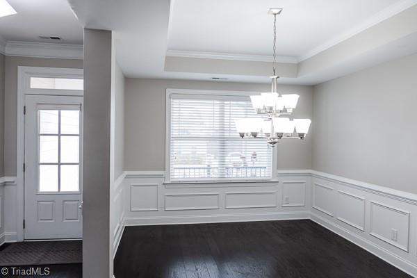 unfurnished dining area with a chandelier, dark hardwood / wood-style flooring, a raised ceiling, and crown molding