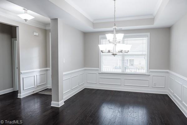 unfurnished dining area with ornamental molding, dark wood-type flooring, a notable chandelier, and a tray ceiling