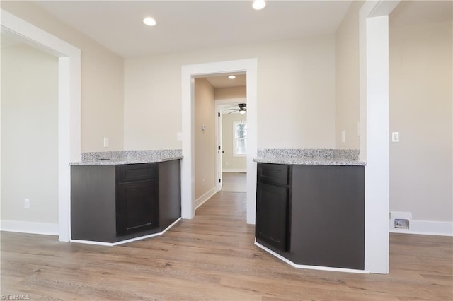 kitchen with ceiling fan, light stone counters, and light hardwood / wood-style floors