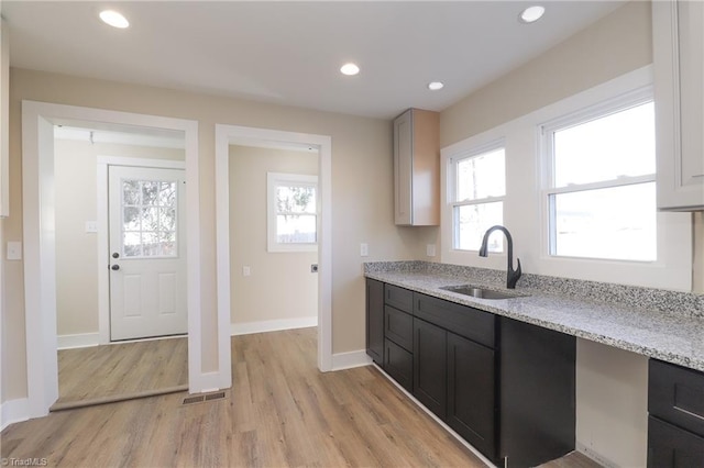 kitchen with light stone countertops, sink, light hardwood / wood-style flooring, and a wealth of natural light