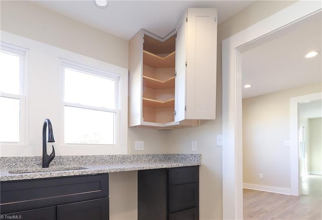 kitchen featuring sink, light stone countertops, white cabinets, and light wood-type flooring