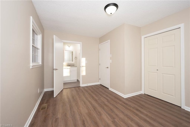 unfurnished bedroom with ensuite bathroom, a closet, dark hardwood / wood-style floors, and a textured ceiling