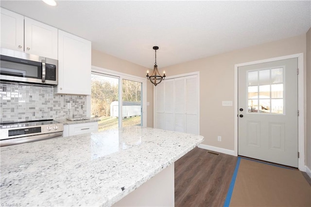 kitchen featuring light stone countertops, backsplash, stainless steel appliances, white cabinets, and hanging light fixtures