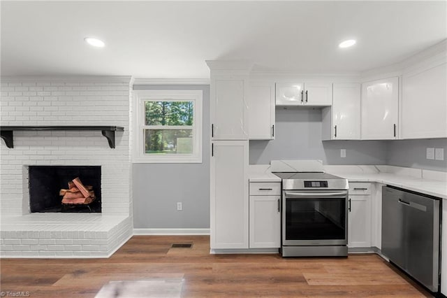 5403 Southmont Dr, Julian, NC 27283 - kitchen featuring appliances with stainless steel finishes, white cabinets, light wood-style flooring, light stone counters, and a fireplace
