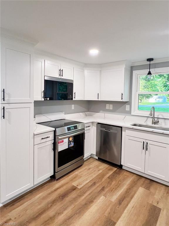 5403 Southmont Dr, Julian, NC 27283 - kitchen with stainless steel appliances, white cabinets, light countertops, light wood-style floors, and decorative light fixtures