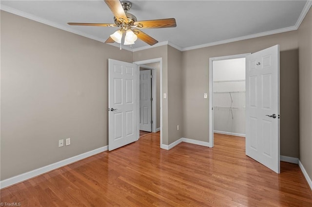 unfurnished bedroom with a closet, crown molding, a spacious closet, light wood-style flooring, and baseboards