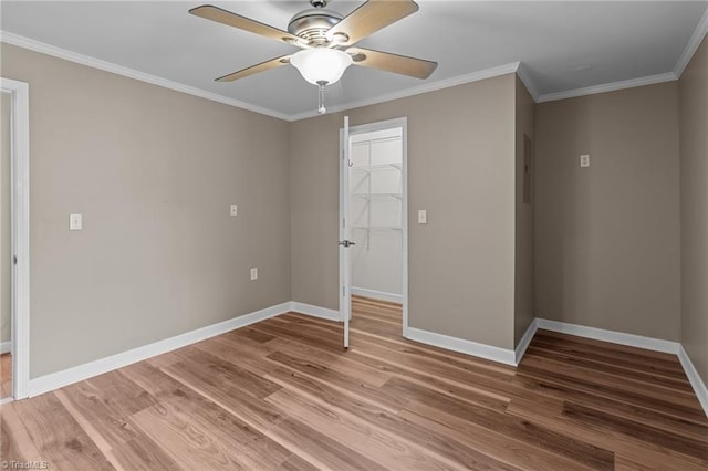 unfurnished bedroom featuring a walk in closet, ornamental molding, baseboards, light wood-style flooring, and a closet