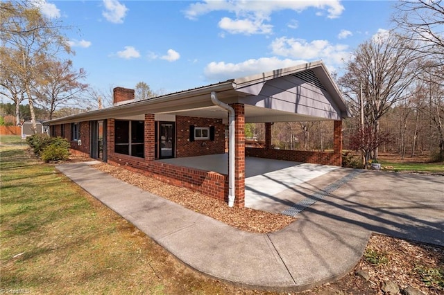 rear view of property featuring a chimney, a lawn, brick siding, driveway, and a carport