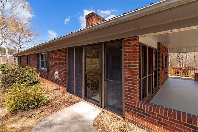 view of exterior entry featuring a chimney and brick siding