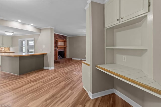 kitchen with baseboards, light wood-style floors, ornamental molding, and a brick fireplace