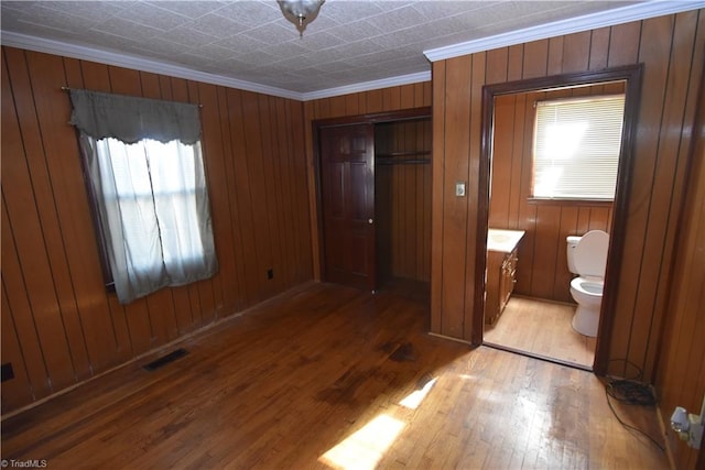 unfurnished bedroom with wood walls, hardwood / wood-style floors, a closet, crown molding, and ensuite bathroom