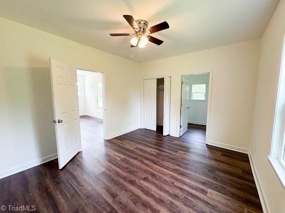 unfurnished bedroom with dark wood-style floors, a closet, baseboards, and a ceiling fan