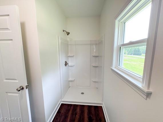 full bathroom featuring a shower, wood finished floors, and baseboards