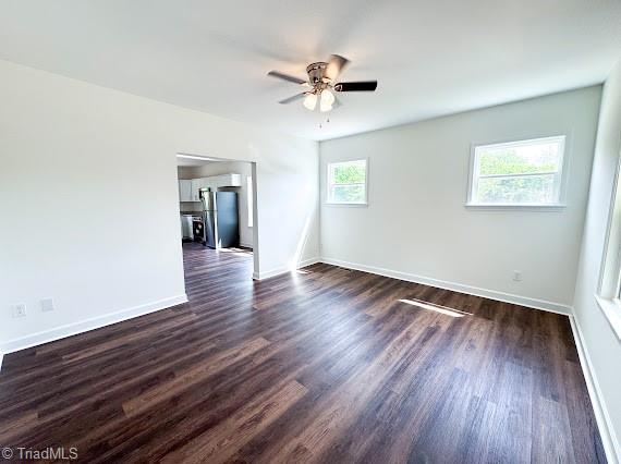unfurnished room featuring a ceiling fan, baseboards, and dark wood-style flooring