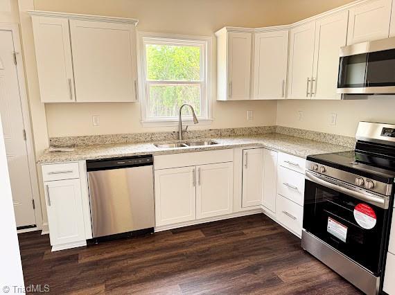 kitchen with stainless steel appliances, a sink, white cabinetry, dark wood-style flooring, and light stone counters