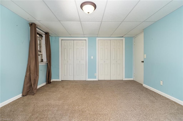unfurnished bedroom with a drop ceiling, carpet floors, baseboards, and multiple closets