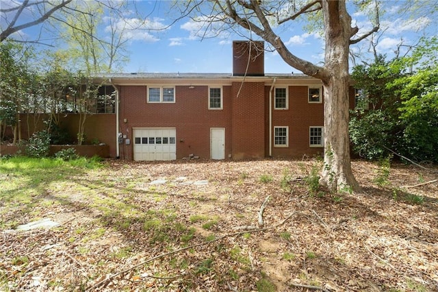 rear view of property featuring an attached garage, a chimney, and brick siding