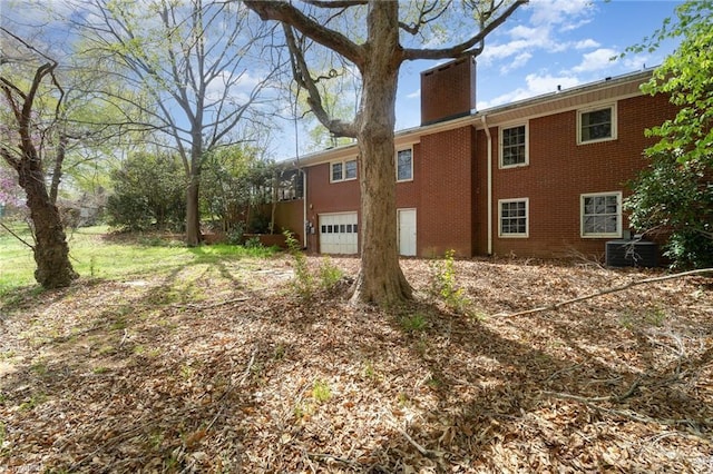 view of side of home with brick siding, a garage, and a chimney