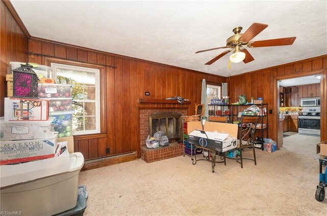 living room featuring wood walls, crown molding, carpet, a brick fireplace, and a ceiling fan