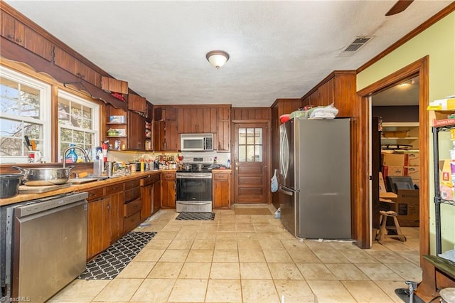 kitchen with open shelves, ornamental molding, stainless steel appliances, a sink, and visible vents