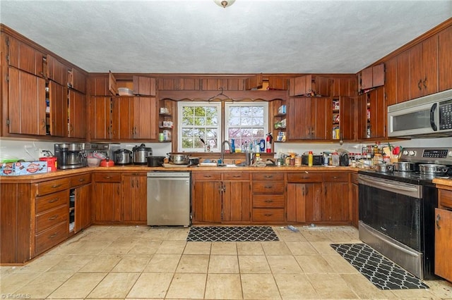 kitchen featuring a sink, stainless steel appliances, brown cabinetry, and open shelves