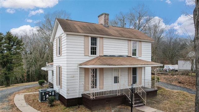 traditional-style home with covered porch, a chimney, central AC, and roof with shingles