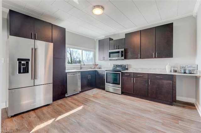 kitchen featuring light wood finished floors, a sink, light countertops, ornamental molding, and appliances with stainless steel finishes