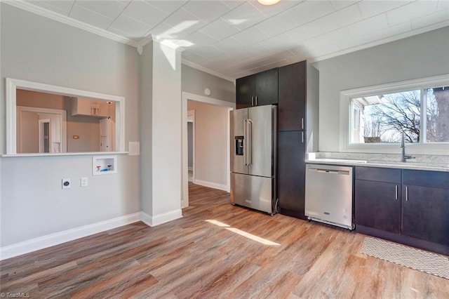 kitchen with light wood-style flooring, a sink, stainless steel appliances, light countertops, and ornamental molding