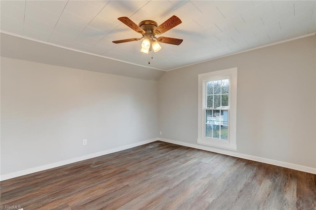empty room with wood finished floors, vaulted ceiling, ceiling fan, baseboards, and crown molding