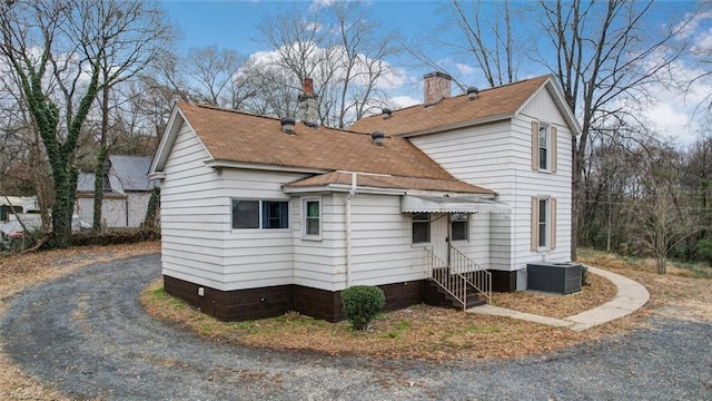 exterior space featuring central air condition unit, a chimney, driveway, and roof with shingles