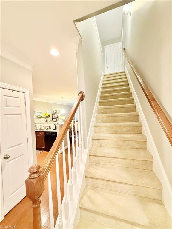 stairway with crown molding, recessed lighting, and wood finished floors