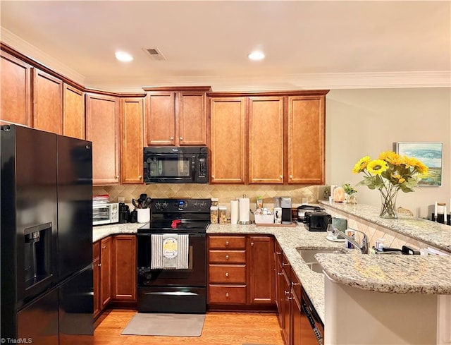 kitchen featuring backsplash, light wood-style flooring, a peninsula, black appliances, and a sink