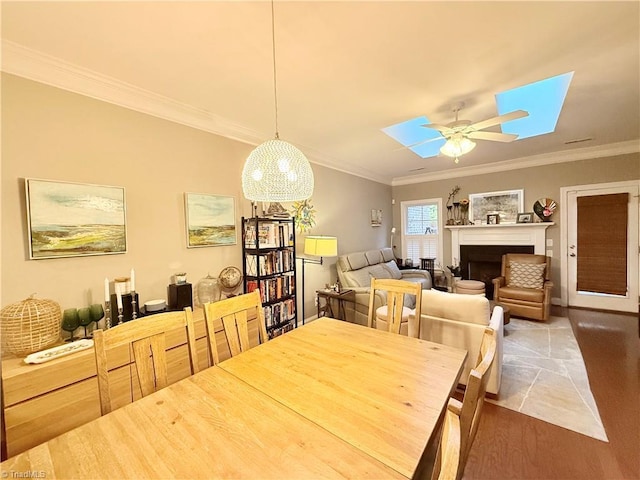 dining room featuring ceiling fan, a skylight, a fireplace, and crown molding