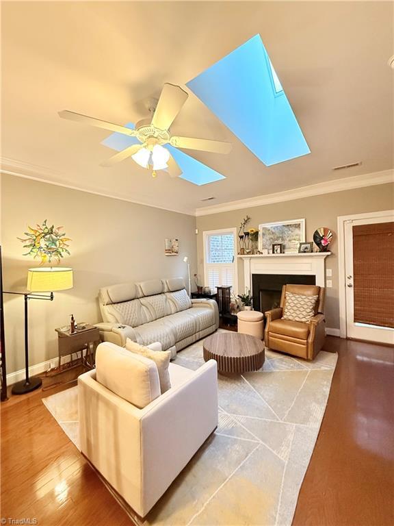 living room with wood finished floors, a skylight, a fireplace, and ornamental molding