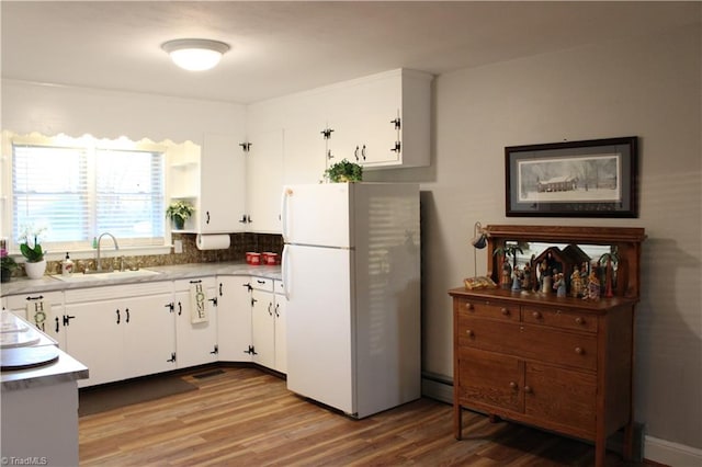 kitchen with backsplash, white refrigerator, sink, light wood-type flooring, and white cabinetry