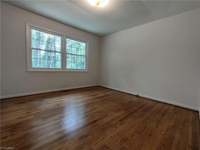 spare room featuring a textured ceiling and dark hardwood / wood-style flooring