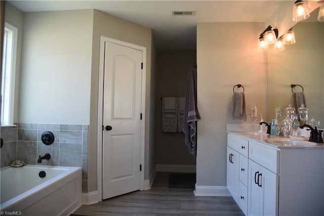 bathroom with visible vents, a sink, wood finished floors, double vanity, and a bath