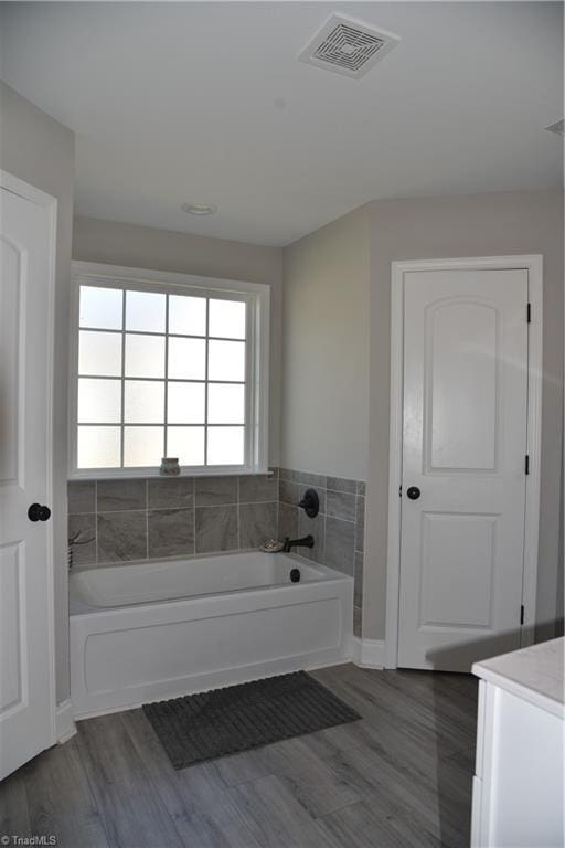 bathroom with a bath, visible vents, and wood finished floors