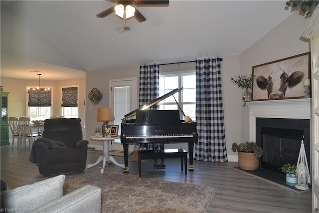 living room featuring wood finished floors, visible vents, lofted ceiling, a fireplace, and ceiling fan with notable chandelier