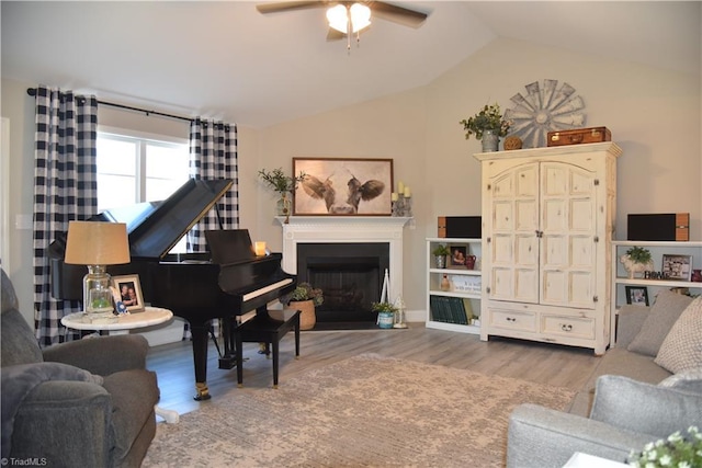 living area with a fireplace, lofted ceiling, ceiling fan, and wood finished floors