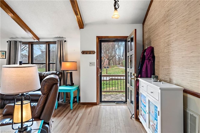 entryway featuring a wealth of natural light, beamed ceiling, light wood-style flooring, and an accent wall