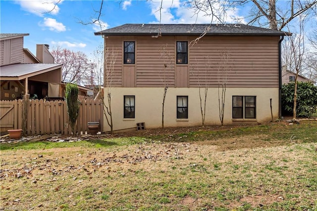 rear view of house featuring a lawn and fence