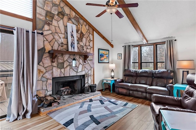 living area with beam ceiling, a stone fireplace, a healthy amount of sunlight, and wood finished floors