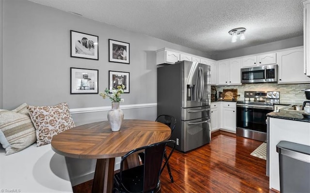 kitchen with stainless steel appliances, dark countertops, dark wood-style flooring, and white cabinetry