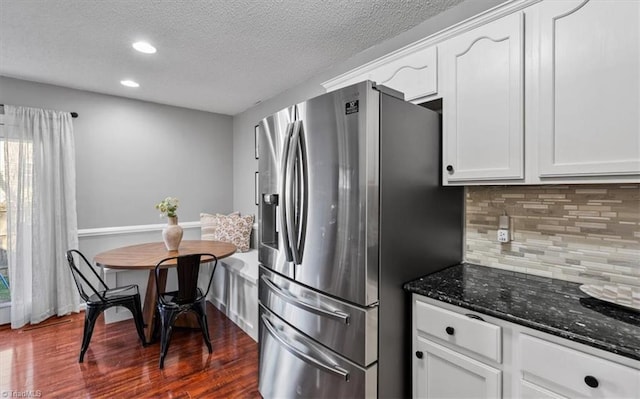 kitchen with dark wood-type flooring, dark stone counters, decorative backsplash, stainless steel refrigerator with ice dispenser, and white cabinets