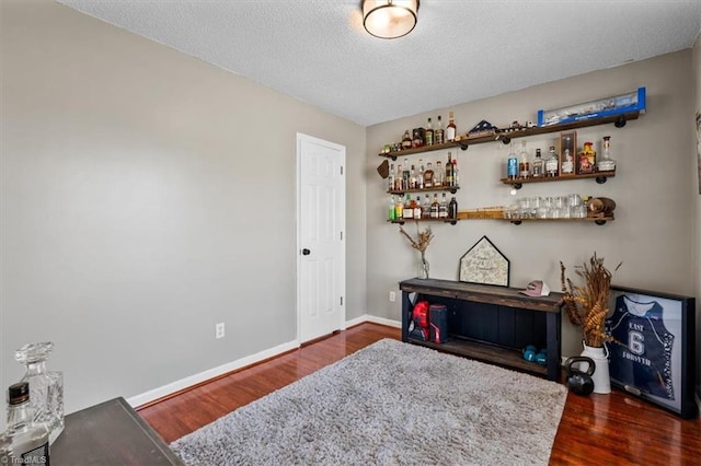 interior space featuring a bar, wood finished floors, baseboards, and a textured ceiling