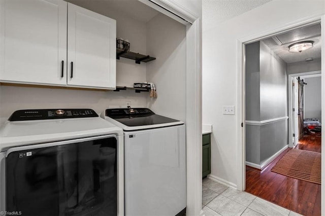 clothes washing area with a textured ceiling, washing machine and dryer, cabinet space, light tile patterned floors, and baseboards