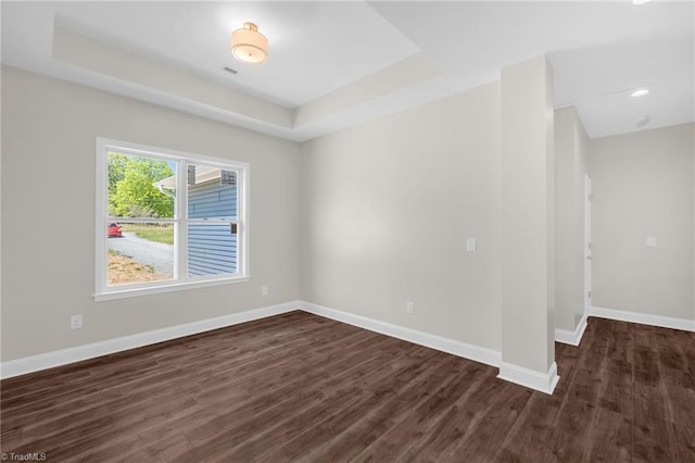 empty room with baseboards, dark wood-style flooring, and a tray ceiling