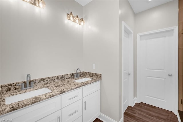 full bath with double vanity, wood finished floors, baseboards, and a sink